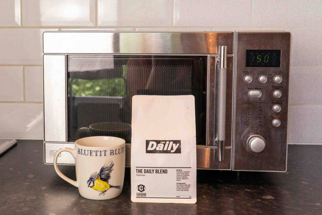 Coffee beans and mug next to a microwave.