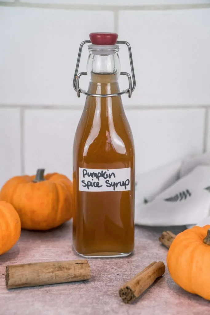 Pumpkin Spice Syrup with pumpkin, cinnamon sticks in the backgroud. 