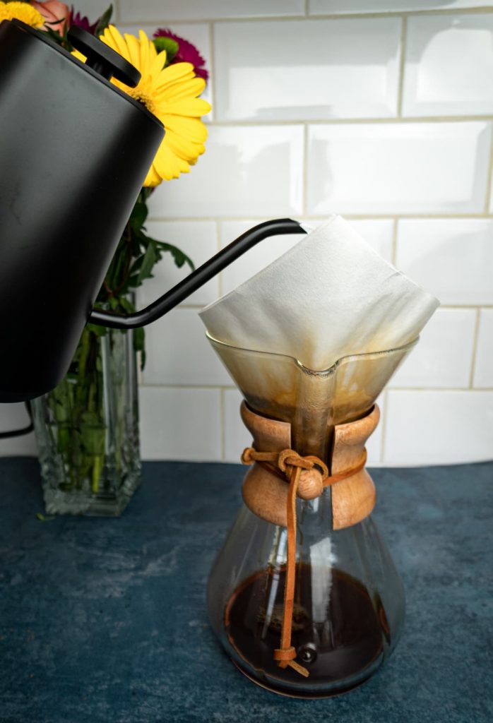 Pouring water in the Chemex to make filter coffee with flowers in the background. 