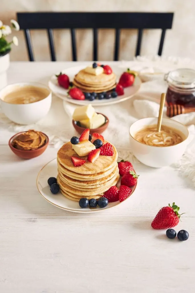 shot of pancakes with fruits on a plate near coffee and syrup at breakfast